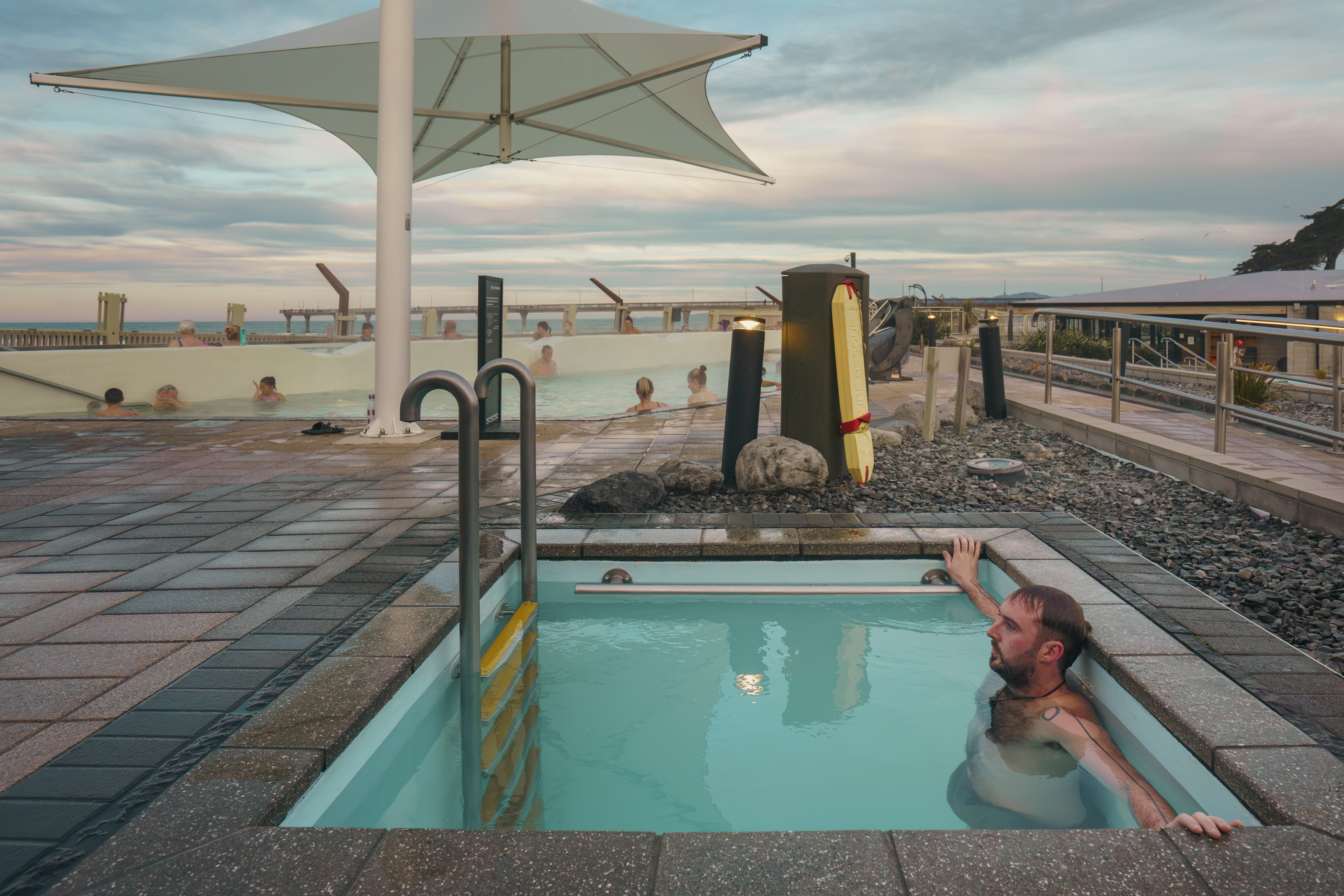 Man sitting in a plunge pool, with people relaxing in a hot pool in the background