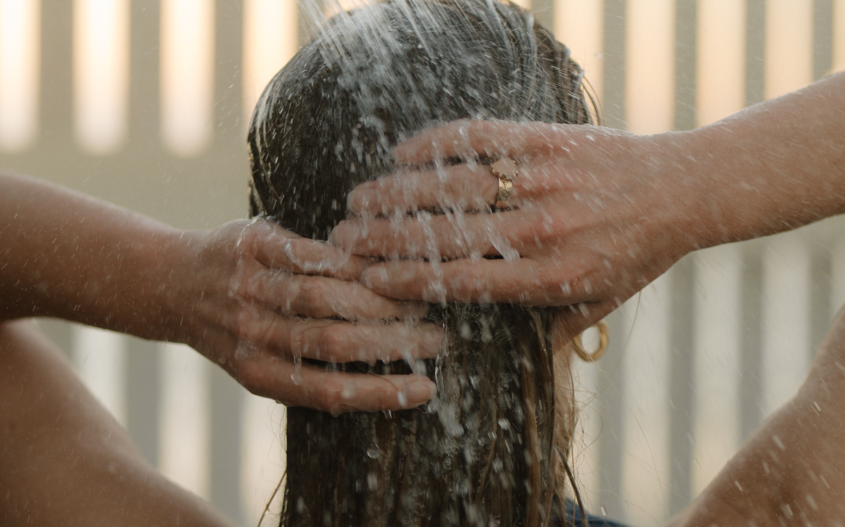 Woman standing in a shower, running her hands through her hair as water falls around her