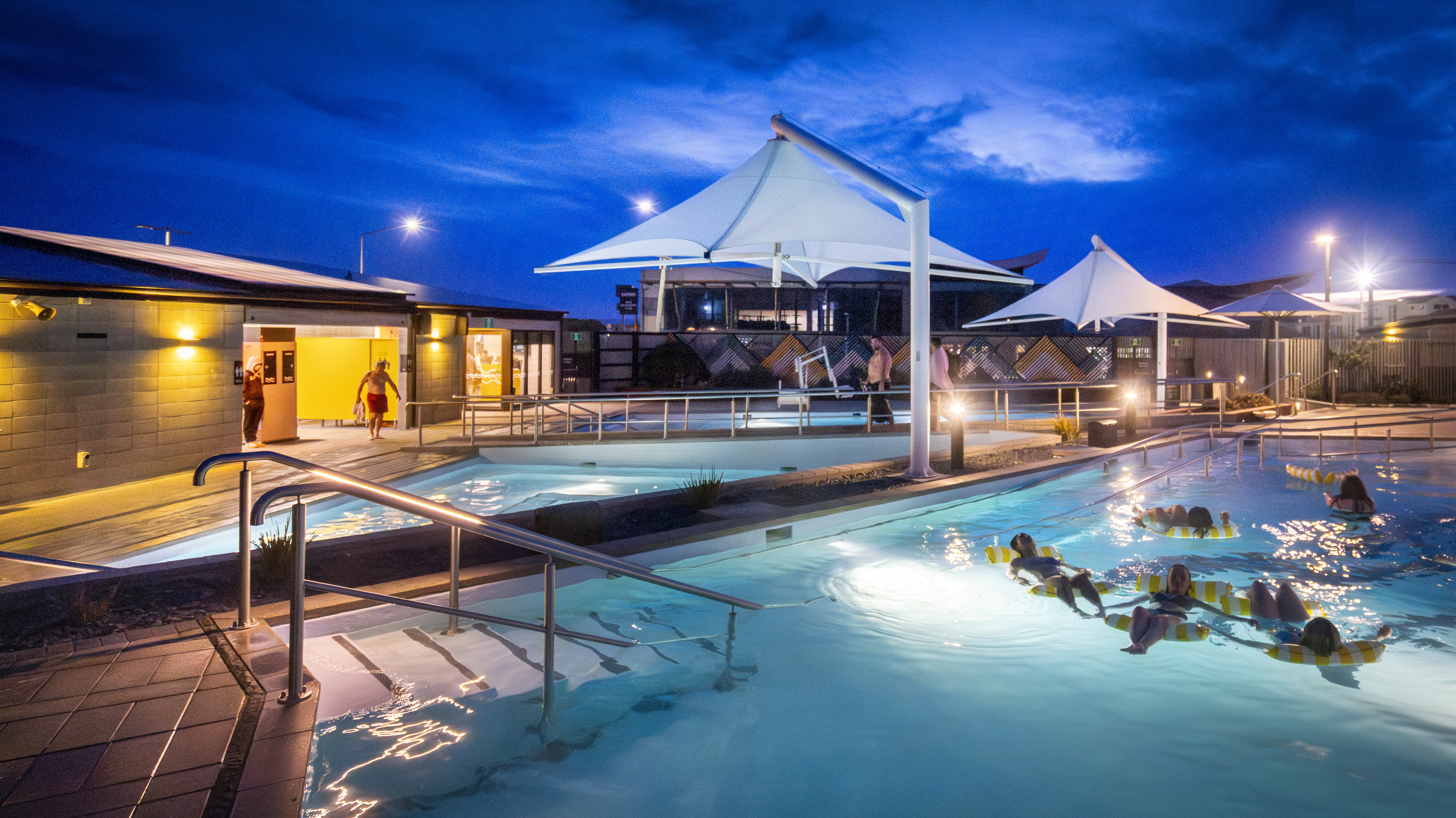 Hot pools at night with people relaxing on inflatable lilos