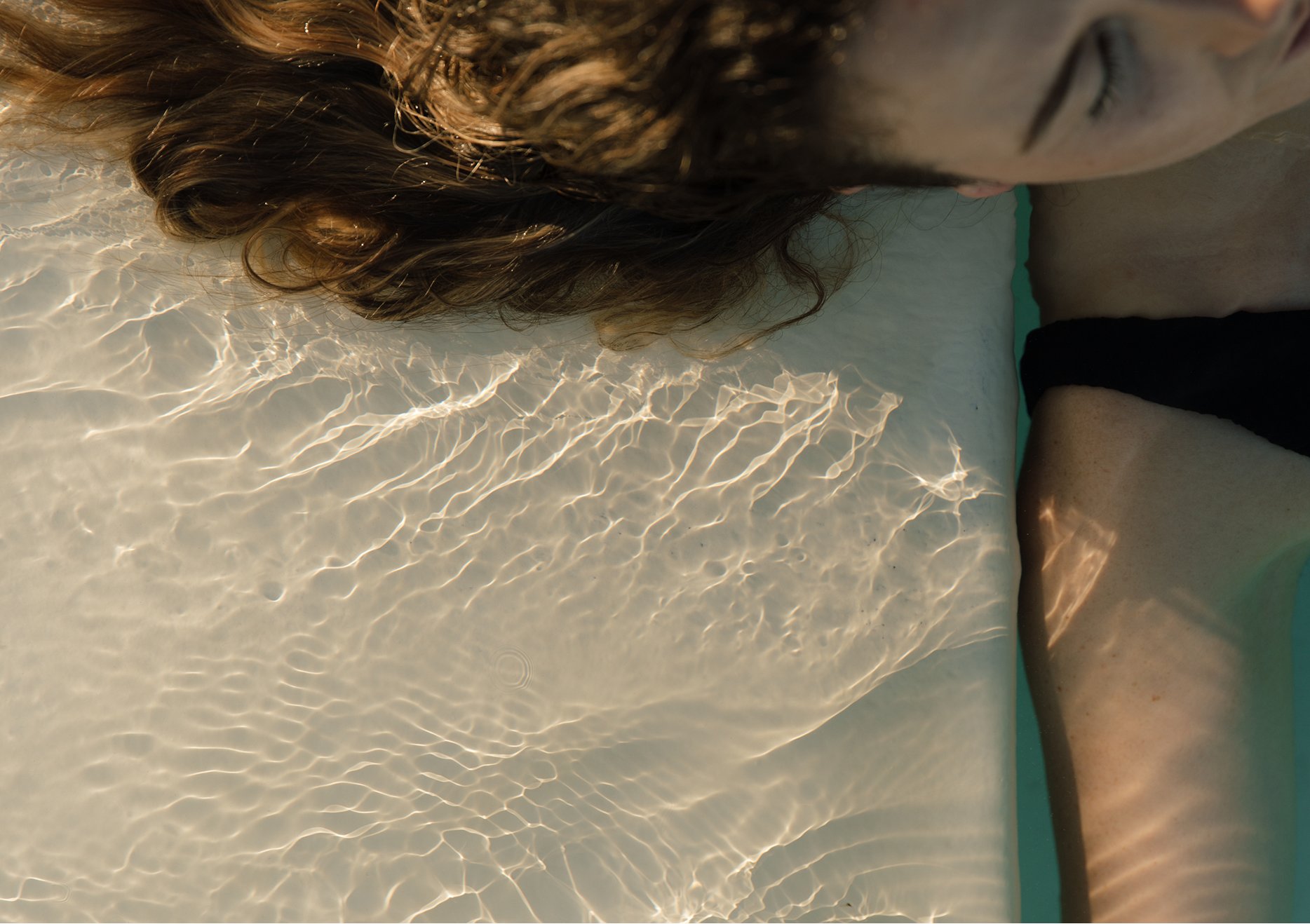 Woman relaxing in a hot pool with her head tilted back, her hair floating on the water's surface as she soaks