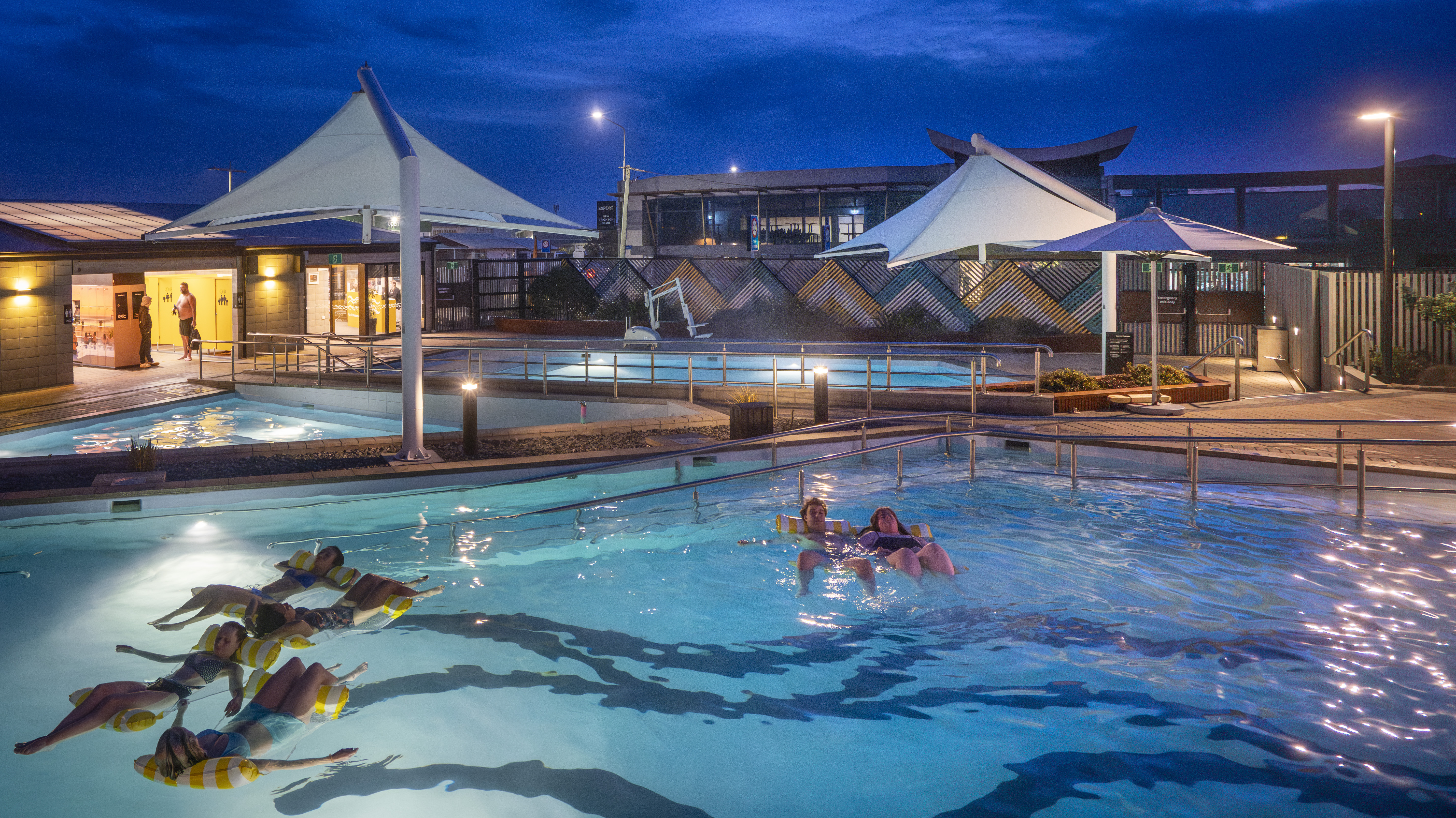 Hot pools at night with people relaxing on inflatable lilos, floating peacefully in the warm water under the evening sky